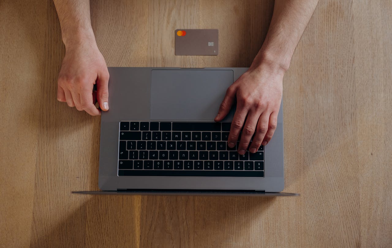 Top view of male hands on a laptop with credit card on wooden table, ideal for online shopping themes.